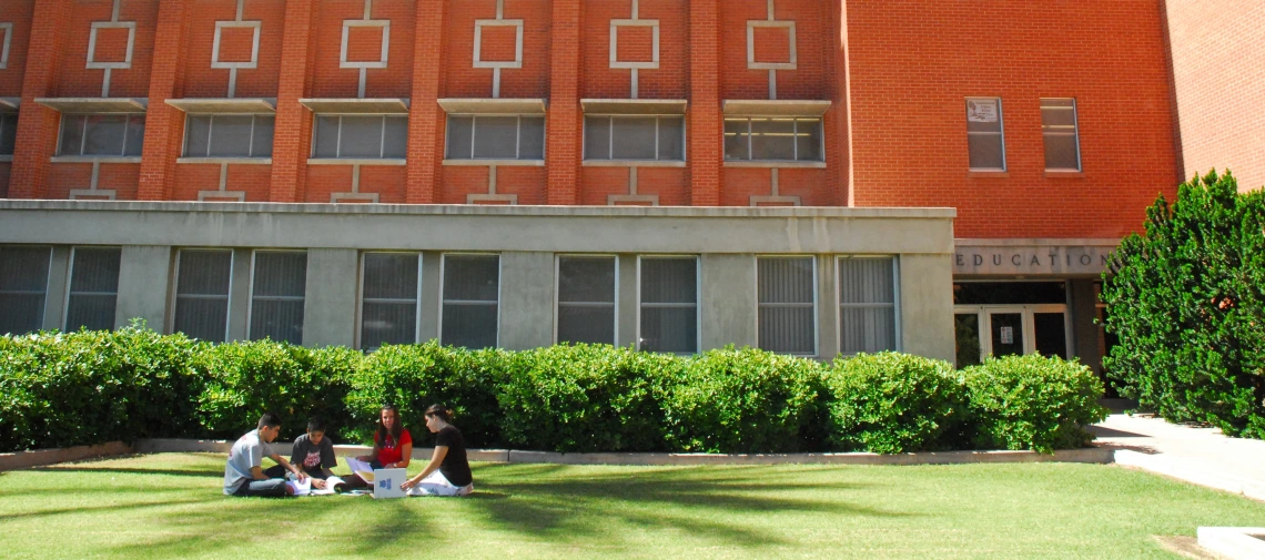coe for web2 032.jpg four students sitting on the lawn in front of the education building on a sunny day